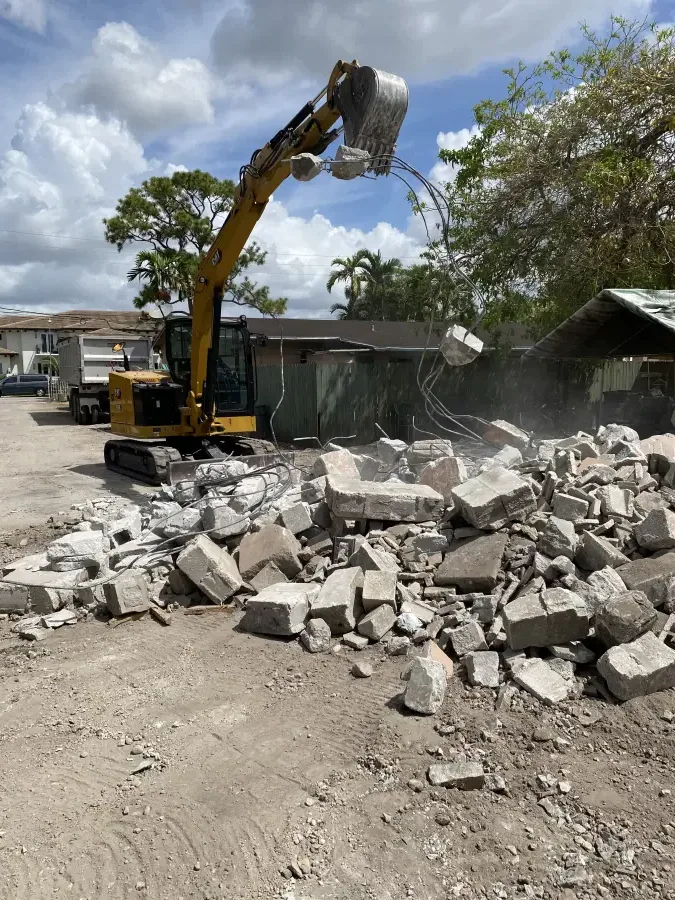 Excavator loading broken concrete into a Waste Masters container at a Miami-Dade job site